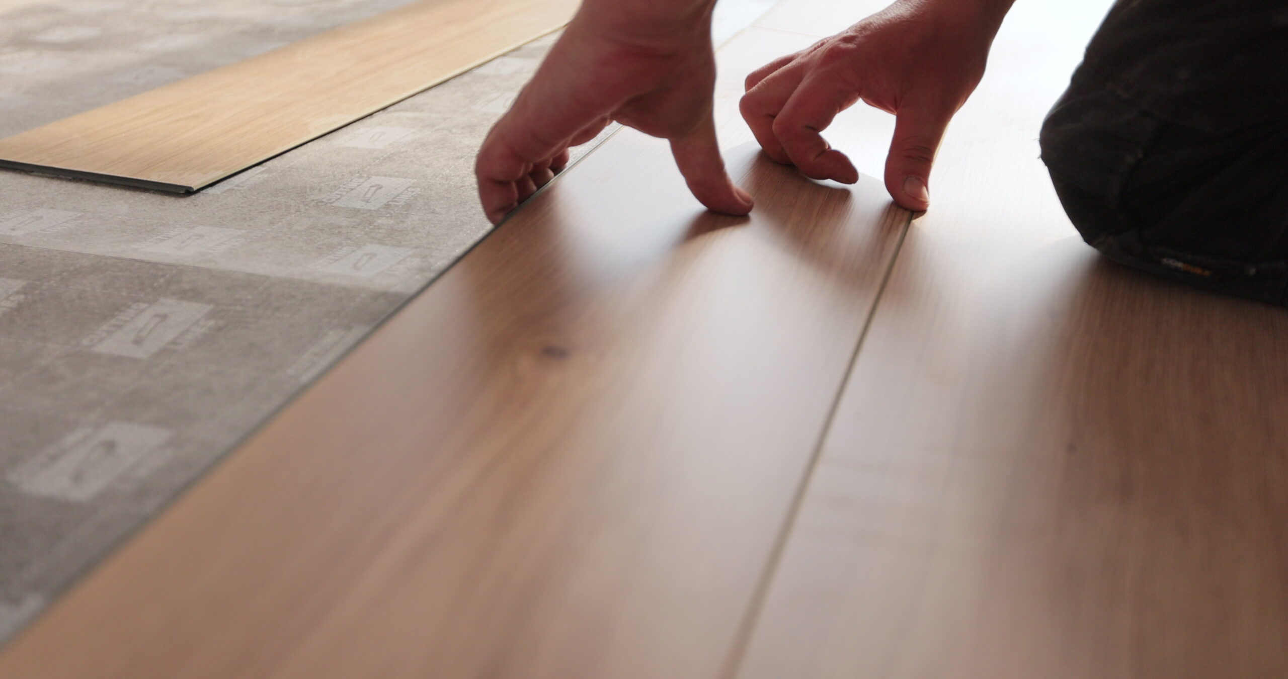 Man kneeling and installing wood laminate floor in a home. Closeup on male hands.